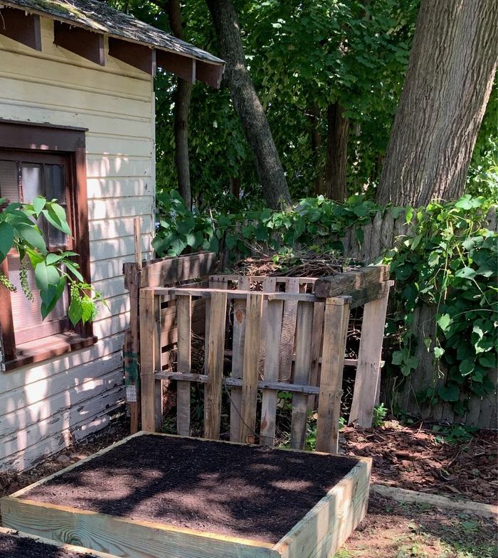 Compost bin made from the right kind of pallets with branches and twigs stuffed between it and the fence