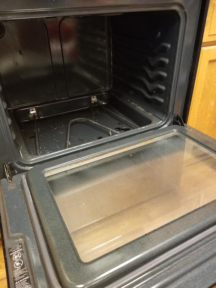 Dirty oven with some debris on the bottom and grease spots on the door