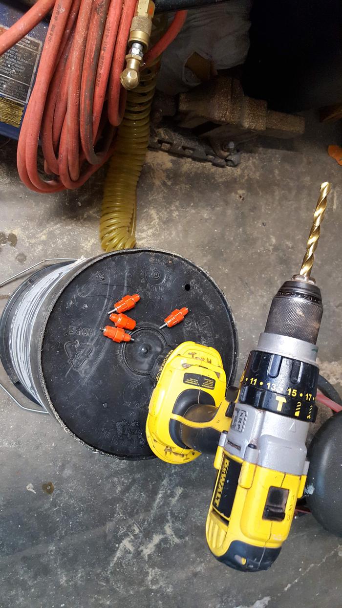 Black 5 gallon bucket with poultry nipples ready to be installed.