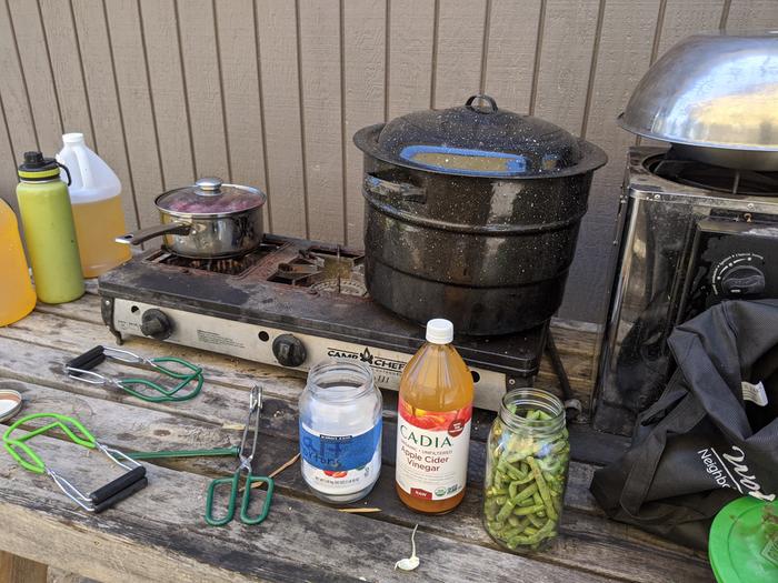 jar of green beans next to vinegar and salt. Hot water bath on stove