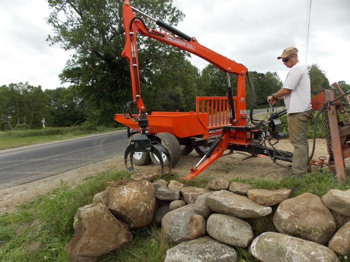 log trailer with grapple lifting rocks into a dump bed