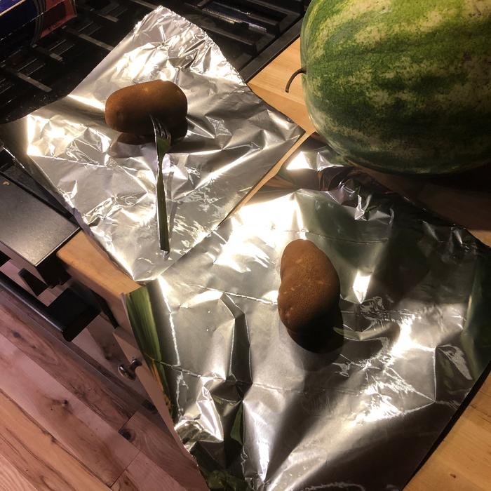 Potatoes stabbed with a fork and getting ready to be rolled up in foil. 