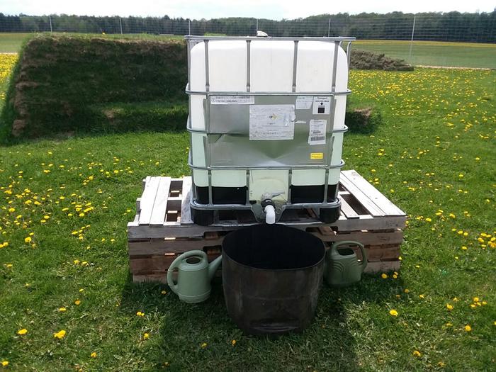 Water totes filled from hydrant with watering cans. Dunk in the balck half barrel for quick filling