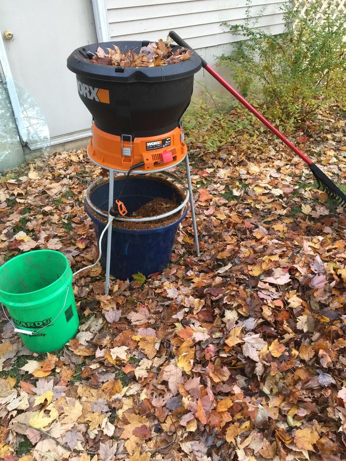 An electric leaf shredder over a bucket of mulch. Rake leans against it