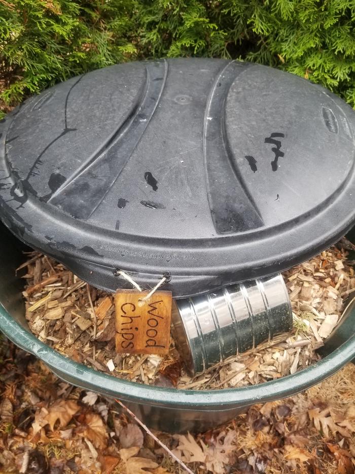 huge garbage can of woodchips with scoop, cover and label 