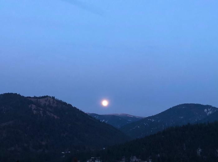 An almost full moon rising over the mountains 