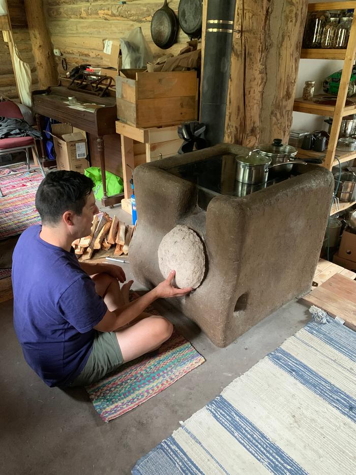 man-in-front-of-cob-covered-rocket-stove-lid