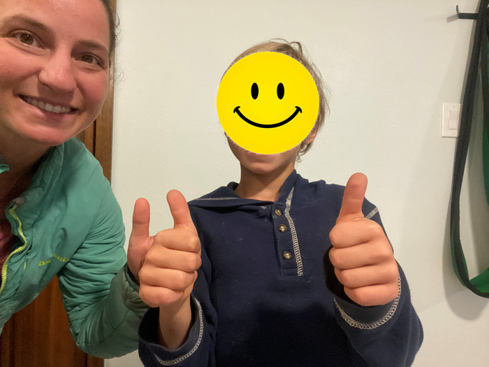 a woman with a boy who is giving two thumbsup in front of a white wall