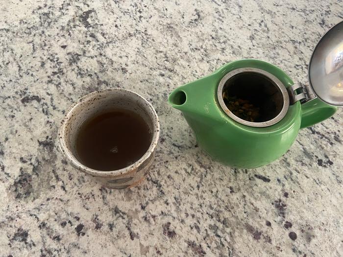 a tea for sore throat made from sage, chamomile, and slippery elm in a tea infuser and a cup on a rock countertop