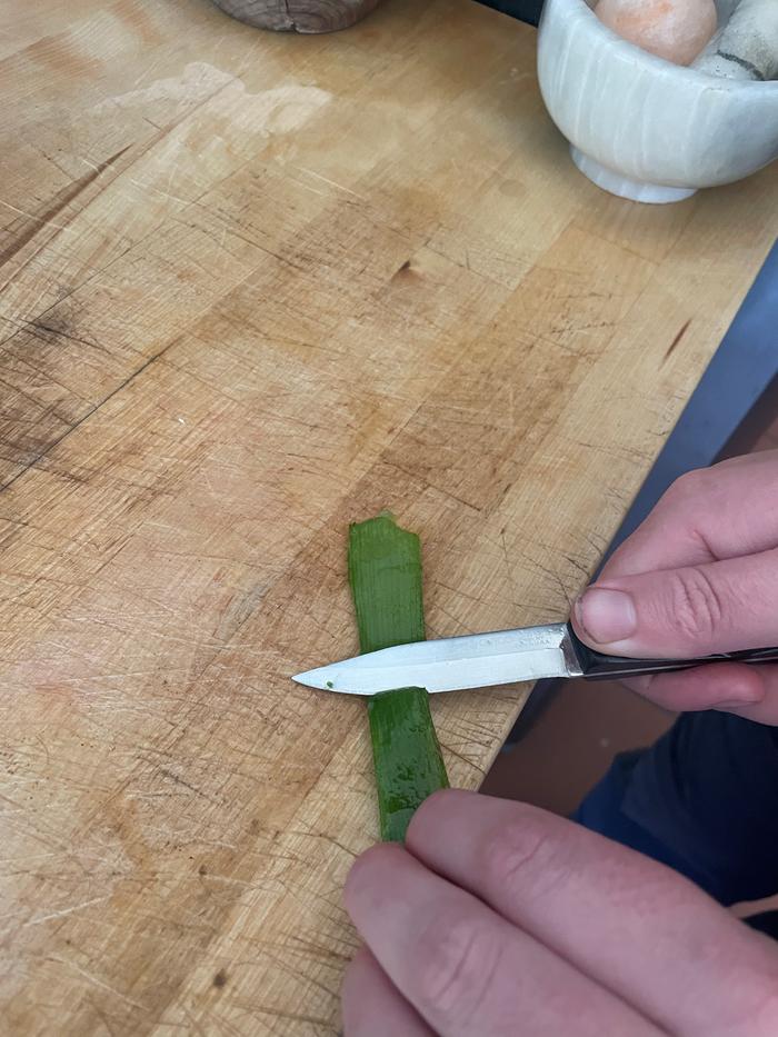 Peeling an aloe leaf with a paring knife on a wood table