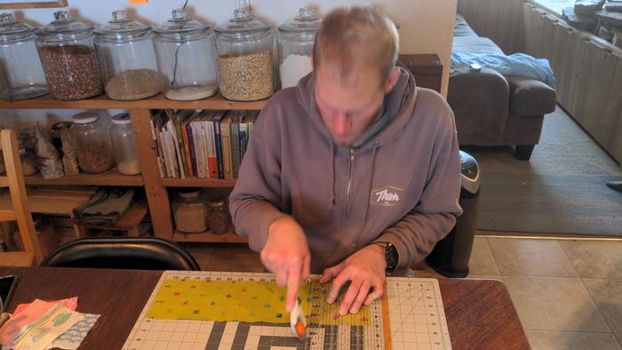 Caleb cutting squares to assemble the new quilt.