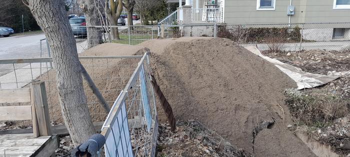 22 tons of sand in a pile in front of a house with a tree and a fence next to it