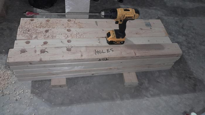 a very long drill bit in a yellow dewalt drill on a pile of short lumber