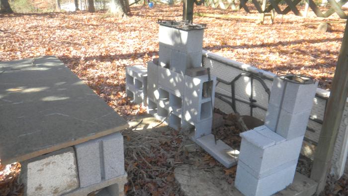 a simple outdoor kitchen of three rocket stove burners made from cinder blocks, leaf covered yard in the background