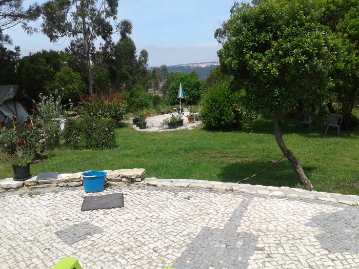 A terrace, trees, yard, bucket and a lower rock paved area against a ridgetop view