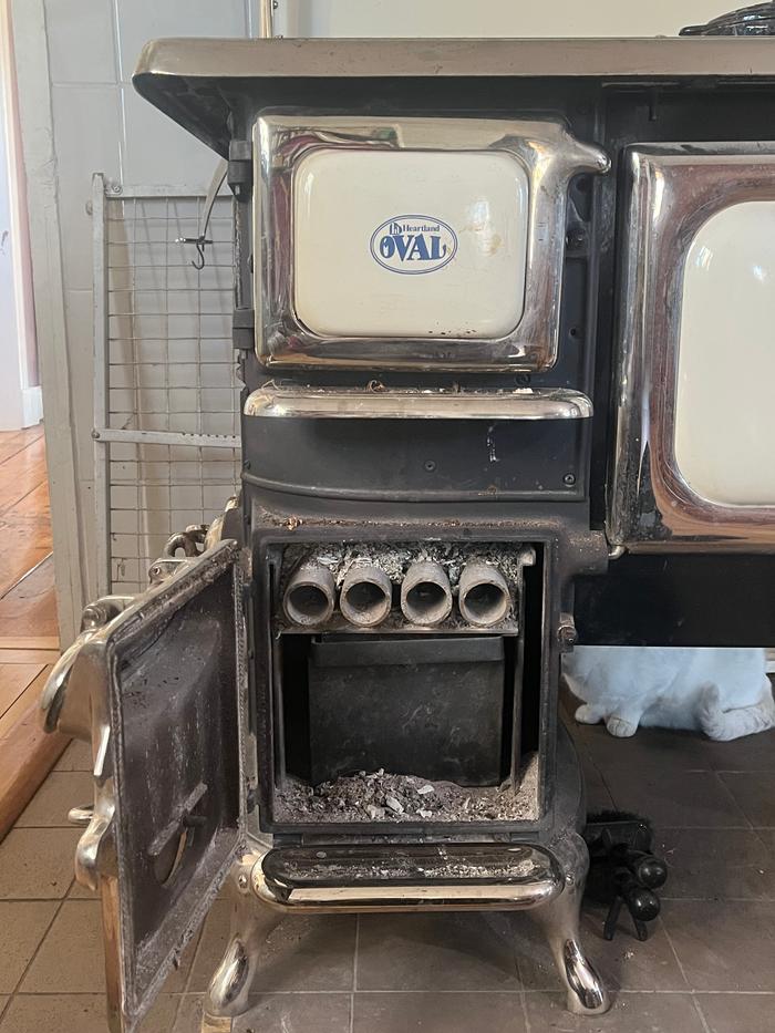 View of our kitchen wood stove with its ash bucket and many year old SS grate pipes