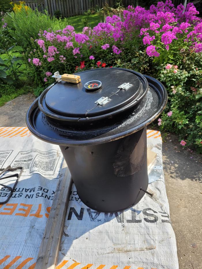 A black barrel with an oven door, thermometer and latch