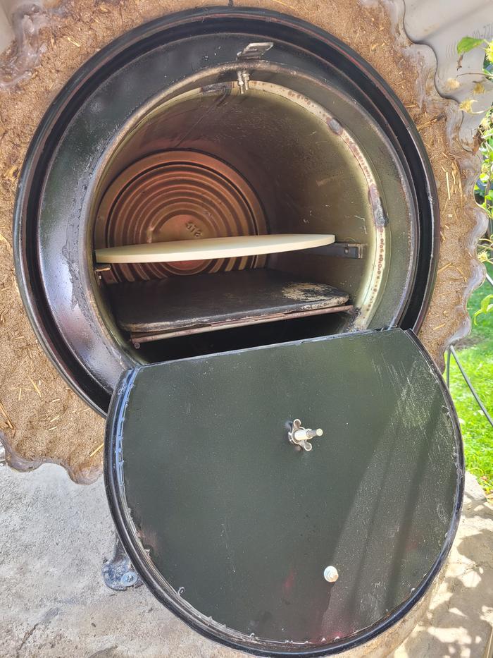 A rocket oven with roofing material outside of insulation material. Racks are inside the oven