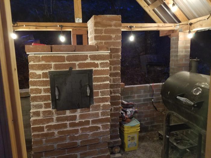 A brick oven and smoker in a brick covered shelter