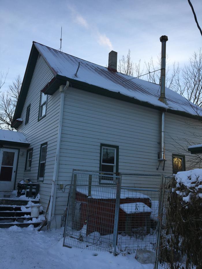 A two story house with a stove pipe that comes out of the wall, heads up through the eaves of the roof and then continues with bracing to hold it up