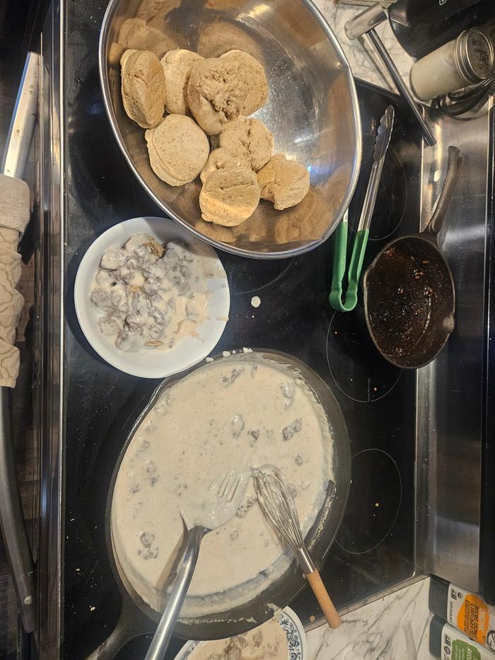 Biscuits in a stainless steel pan, gravy in a wide cast iron skillet, all on a flat electric stovetop