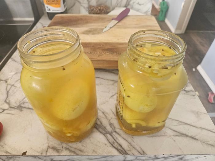 Two glass jars with pickled duck eggs in them on a rock countertop