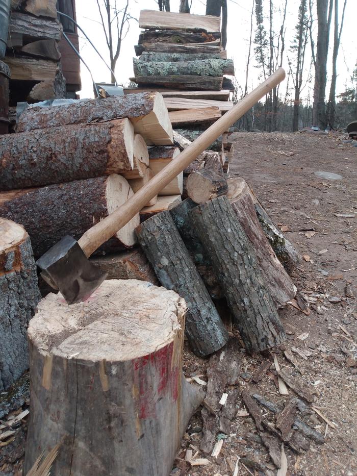 axe in a chopping block in front of a pile of firewood