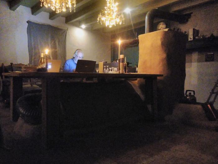 A man with a laptop at a kitchen table warming his feet on the rocket masonry heater under the table