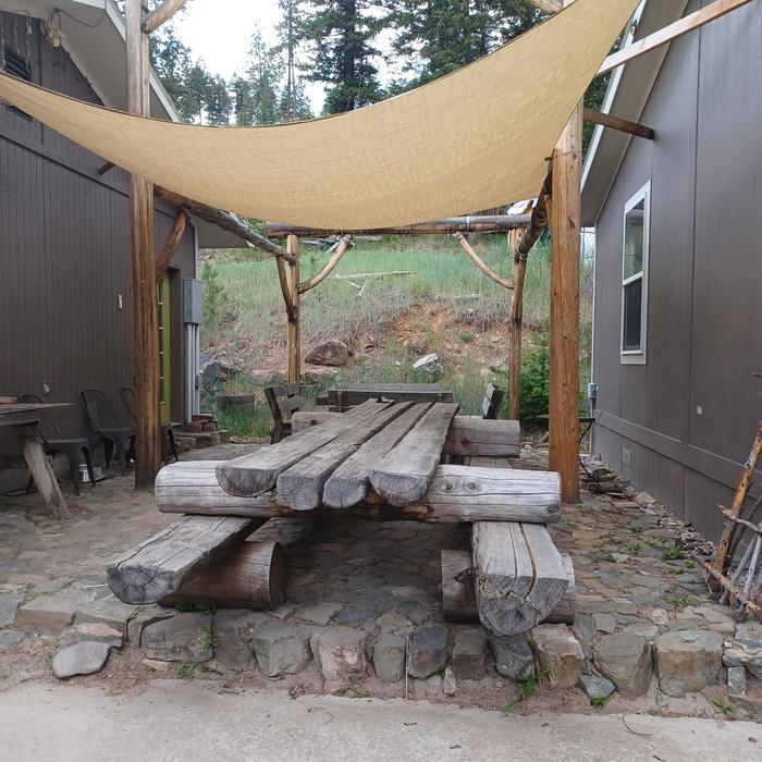 A shade sail over log picnic table 3.0 on a rock patio between two buildings