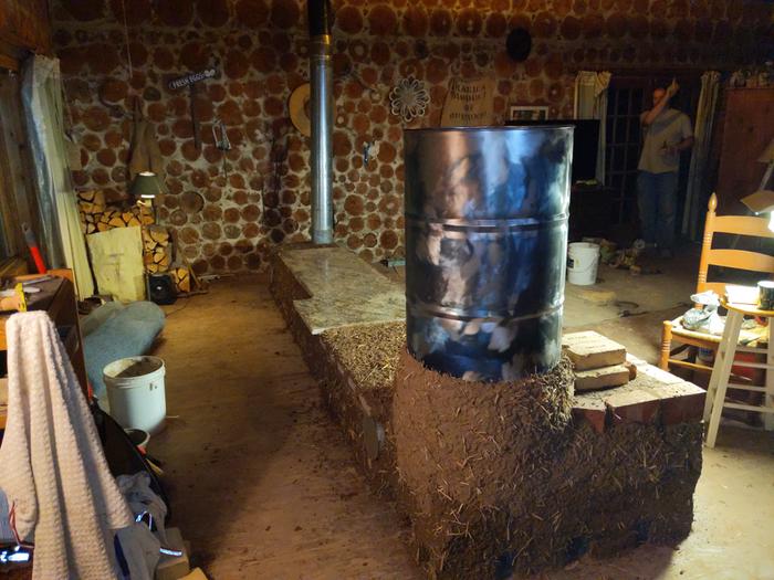 An RMH with rough cob in a cordwood cabin. A man to the right points up towards the ceiling