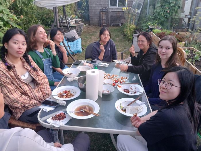 women round a table outside eating plums