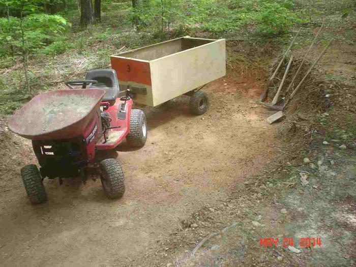 A lawnmower with a wheelbarrow mounted on the hood. Open the hood to dump