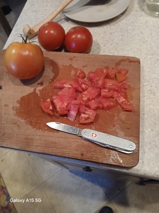 a tomato on a cutting board next to pieces of a tomato that were cut up by a swiss army knife