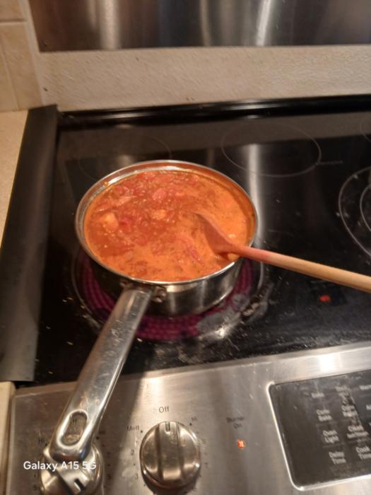tomato sauce cooking on a flat top stove in a stainless steel pot with a wooden spoon in it