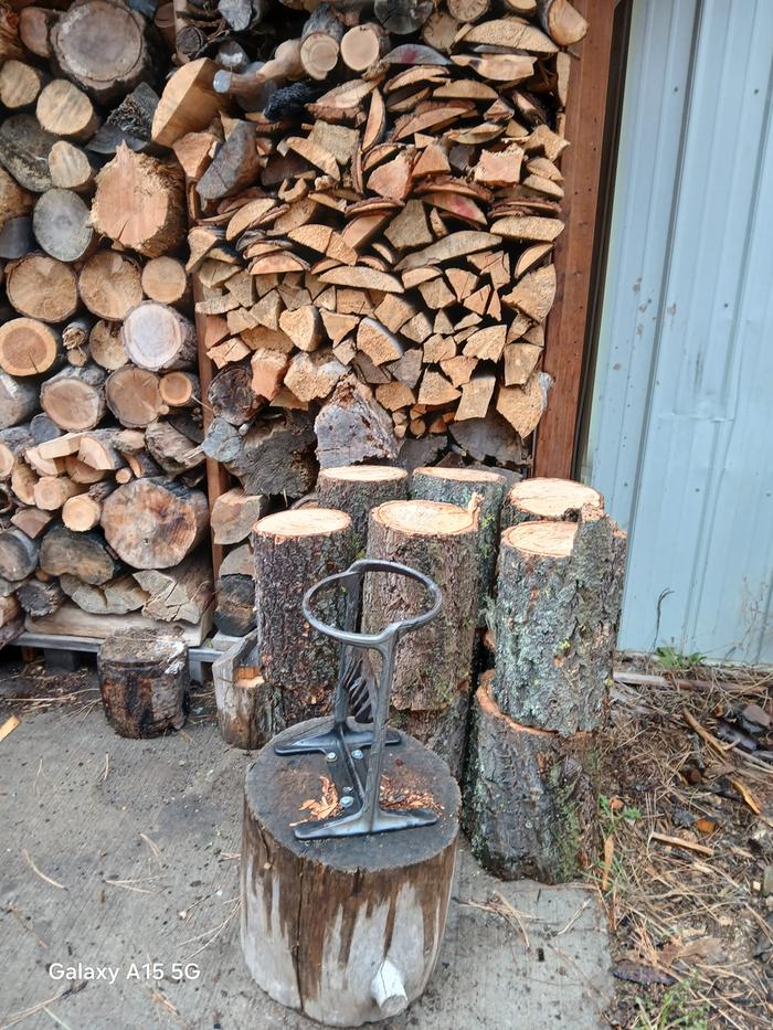 a kindling cracker, rounds of firewood and stacked firewood against a building