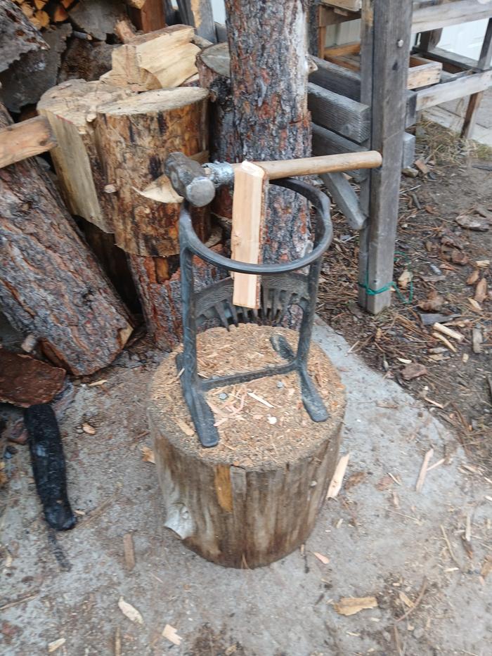 firewood partly split in a kindling cracker with a small sledgehammer and more firewood stacked behind it