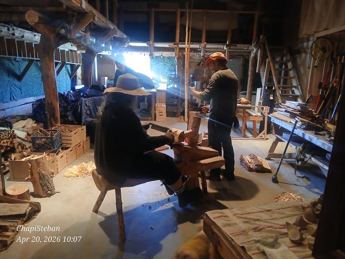 Two people in a shop splitting shakes and shaping wood with a drawknife