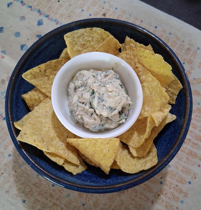A mayonnaise and greens dip or spread surrounded by tortilla chips