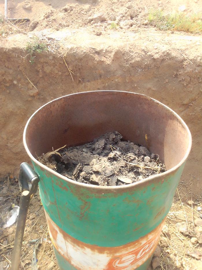 soil, grass and ash in a drum close to one of the pit's corner where I will put a banana tree