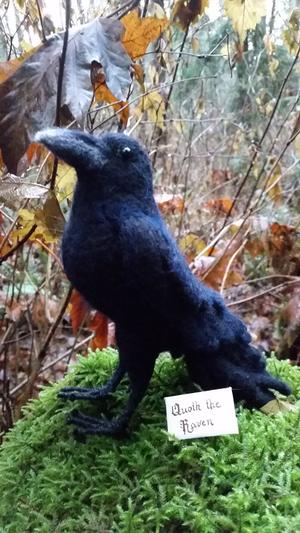 Wool Raven figurine on a mossy log in the woods with a tiny envelope that reads quoth the raven