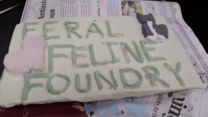 clay sign reading feral feline foundry that is in the process of being glazed