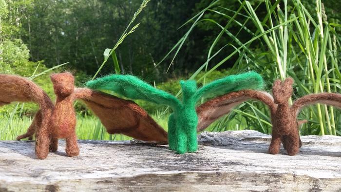 Needle felted dragon on a log bench, with verdent nature in the background.